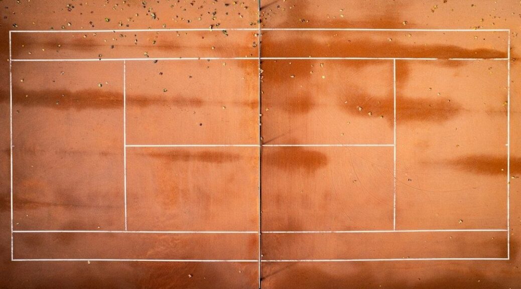 Översikt av en sliten tennisbana med grus och tydliga linjer