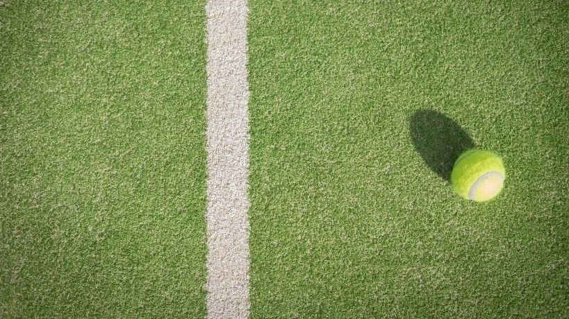 Tennisboll på konstgräs intill en vit linje, med tydlig skugga